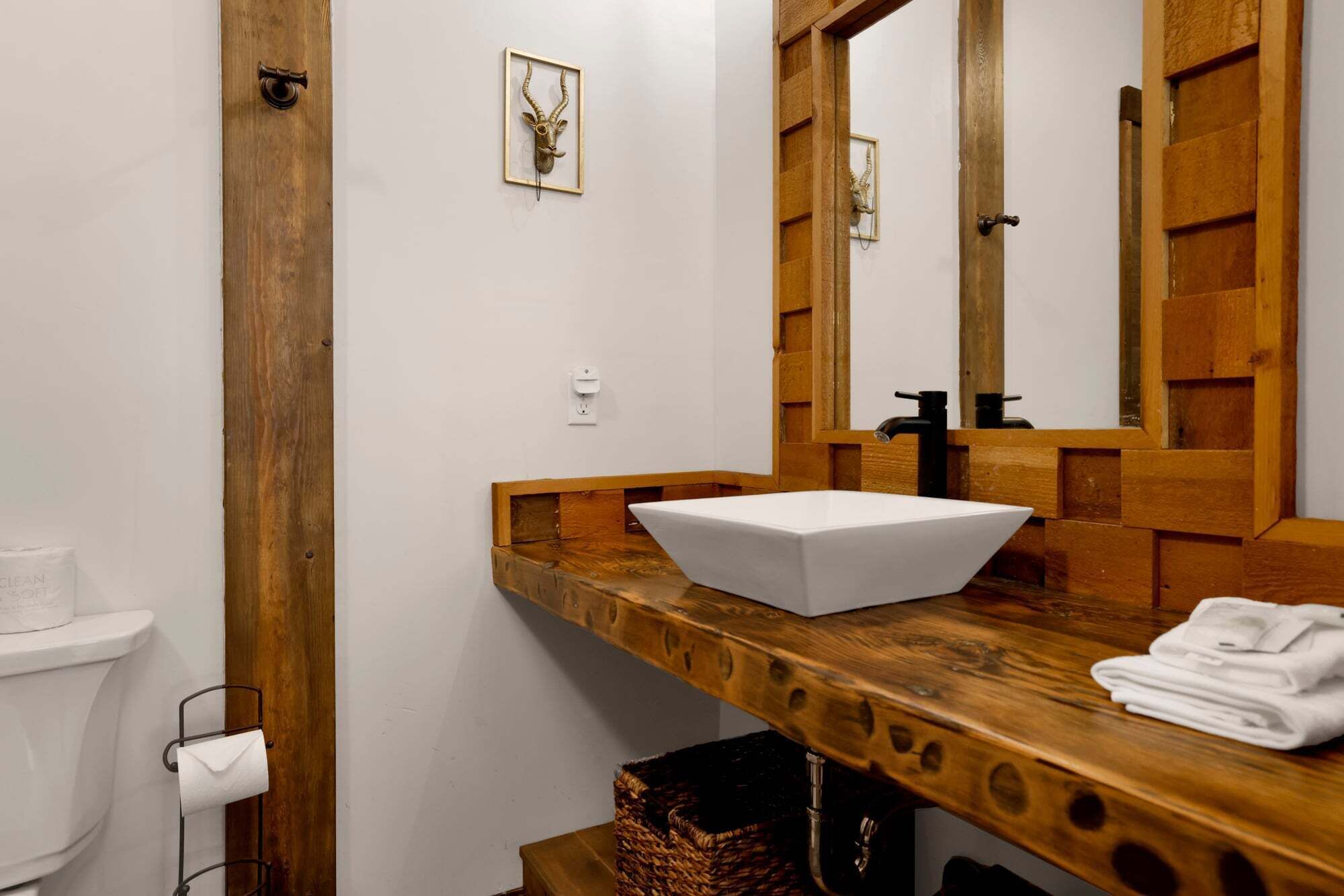 A bathroom with a wooden vanity, a white sink, a mirror, and a toilet.
