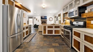 Una cocina moderna con electrodomésticos de acero inoxidable, muebles de madera y suelo de baldosas de piedra.