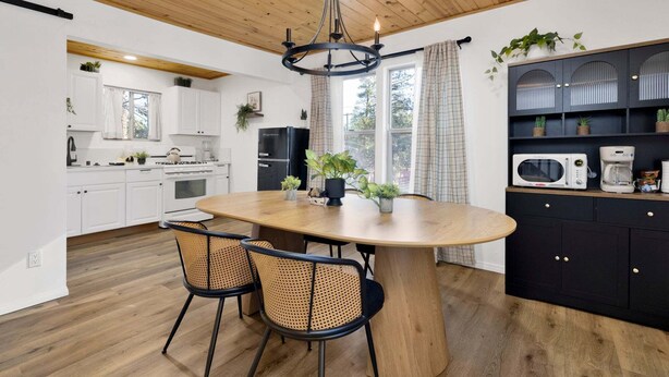 A modern kitchen with white cabinets, a black refrigerator, and a wooden dining table with two chairs. - 2613-shiloh Woods Cabin (Big Bear Lake)