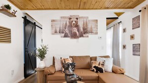 A cozy living room with a brown leather sofa, a bear statue, and a bear-themed wall art. - 2613-shiloh Woods Cabin (Big Bear Lake)