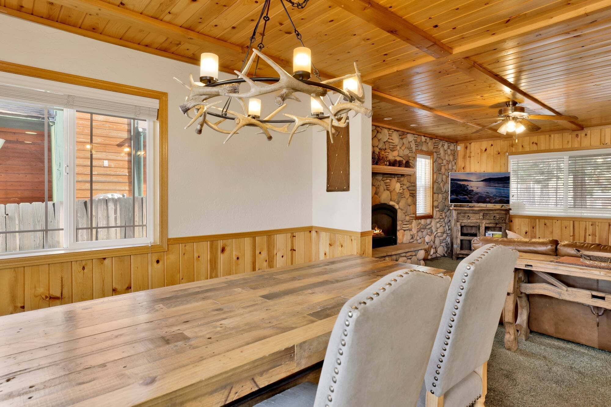 A wooden interior with a stone fireplace, a wooden dining table, and a chandelier with multiple lights.