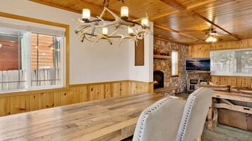 A wooden interior with a stone fireplace, a wooden dining table, and a chandelier with multiple lights.