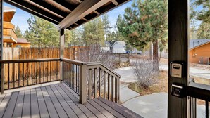 A wooden deck with a railing, a stone wall, and a view of surrounding houses and trees. - Brownie Resort #2618 (Big Bear Lake)