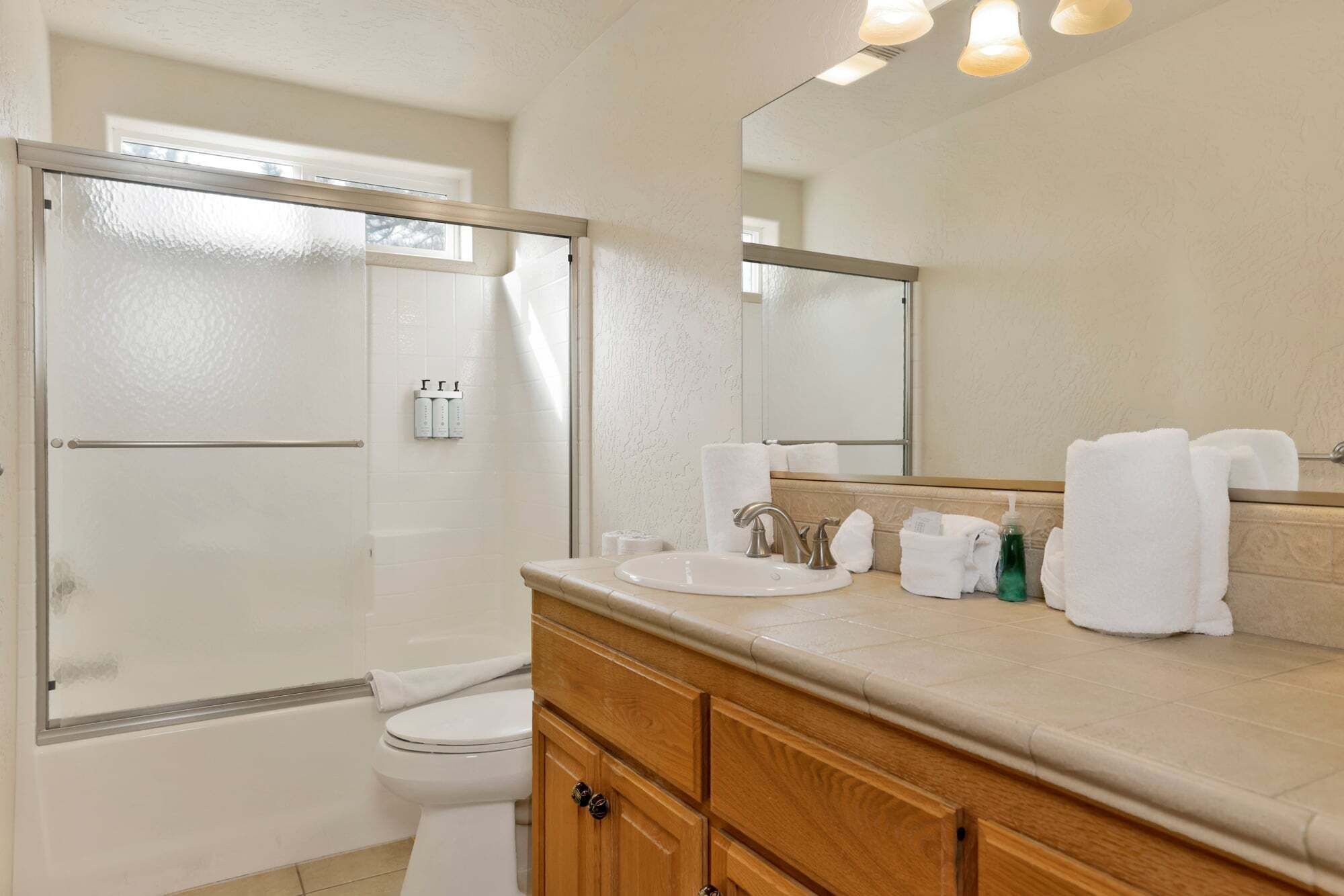 A bathroom with a shower, toilet, sink, and mirror.