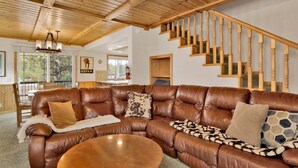 Un salon spacieux avec un grand canapé d’angle en cuir marron, une table basse ronde et un escalier en bois.