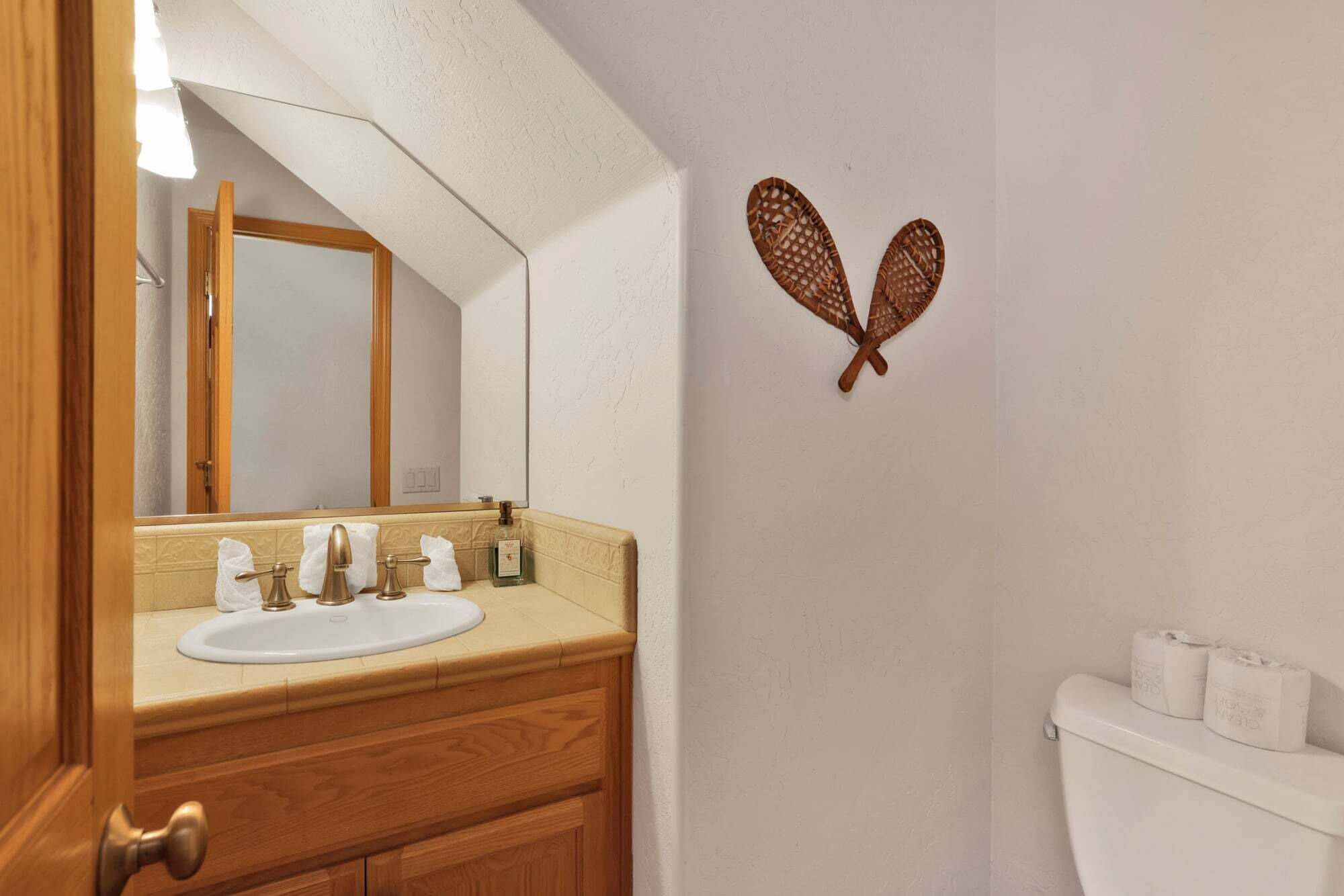 Un baño con tocador de madera, un lavamanos blanco, un espejo y un inodoro con papel higiénico.