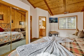 Ein Schlafzimmer mit Holzboden, einem Bett mit Blumenmuster-Bettwäsche, einem Schminktisch, einem Nachttisch und einem Fenster mit Jalousien.