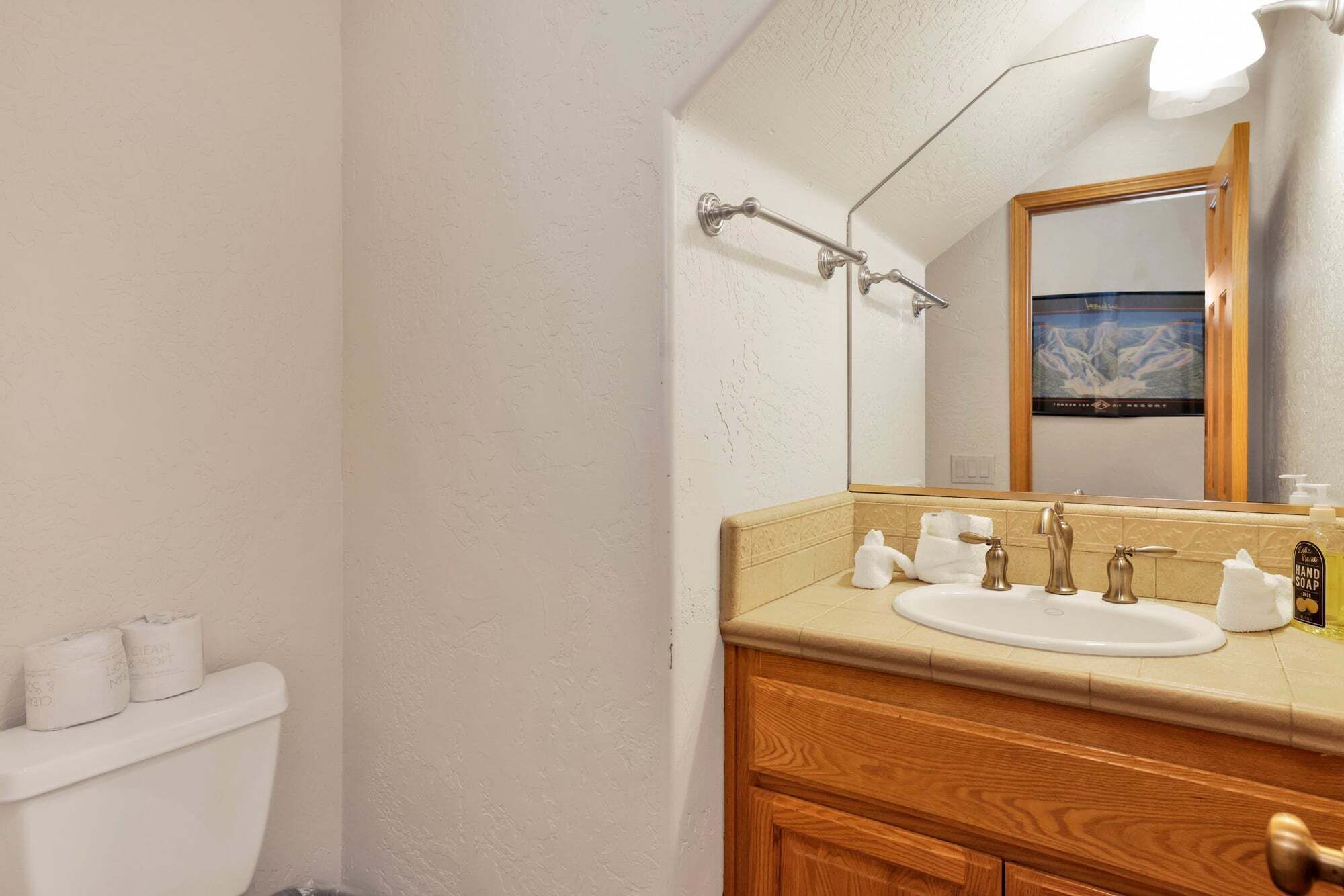 Un baño con inodoro blanco, lavabo con espejo y tocador de madera.