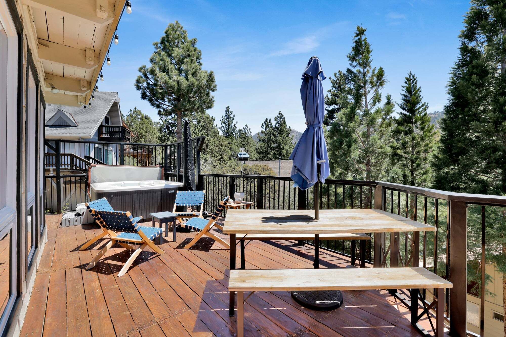 Una terraza de madera con mobiliario exterior, una bañera de hidromasaje y vistas a árboles y montañas.
