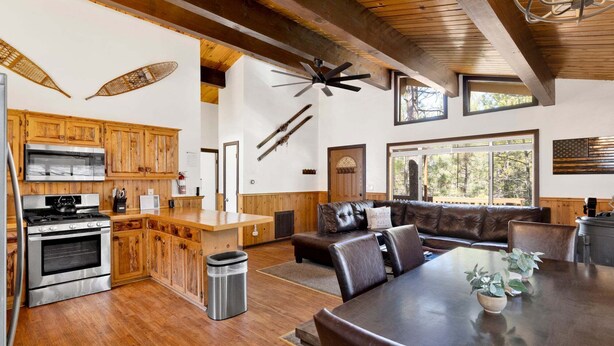 A spacious kitchen with wooden cabinets, a large dining table, and a cozy seating area with a leather couch. - 2655 - Highland Hideout (Big Bear Lake)