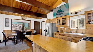A cabin-style kitchen with wooden cabinets, a stainless steel refrigerator, and a dining area with a wooden table and chairs. - 2655 - Highland Hideout (Big Bear Lake)