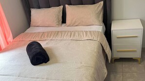 A neatly made bed with a dark headboard, two pillows, and a rolled towel. Adjacent is a white bedside table with drawers. - Charming 3-bedroom House Rental in Centurion, South Africa (Centurion)