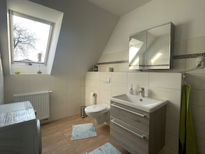 Un baño moderno con ventana, radiador, inodoro, lavabo y espejo.