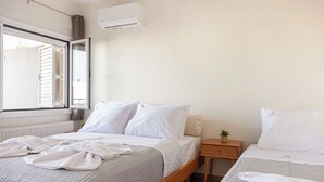 Slaapkamer met twee bedden, een raam met zonwering, een nachtkastje met een plant en een airconditioning.