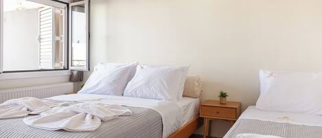 A bedroom with two beds, a window with blinds, a bedside table with a plant, and an air conditioning unit.