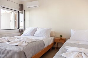 A bedroom with two beds, a window with blinds, a bedside table with a plant, and an air conditioning unit. - Anemelo Cosy Suite 5 Minutes Walk From The Beach (Stalida)
