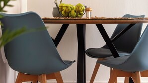 Een eethoek met een houten tafel, twee blauwe stoelen, een wandklok en een vaas met bloemen.