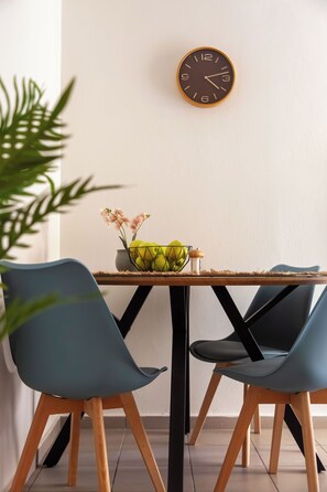 A dining area with a wooden table, two blue chairs, a wall clock, and a vase with flowers. - Anemelo Cosy Suite 5 Minutes Walk From The Beach (Stalida)