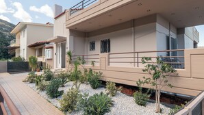 Een modern huis met twee verdiepingen, een balkon, een tuin met verschillende planten en een geplaveid pad.