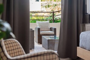 A balcony with wicker furniture, a cushioned chair, and a glass table. - Anemelo Cosy Suite 5 Minutes Walk From The Beach (Stalida)