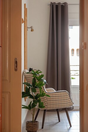 A room with a door, a potted plant, a chair, a curtain, and a view of the outside. - Anemelo Cosy Suite 5 Minutes Walk From The Beach (Stalida)