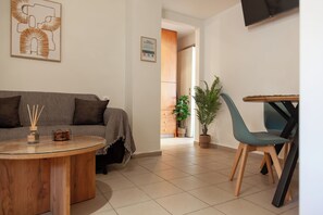 Ein modernes Wohnzimmer mit einer Couch, einem runden Couchtisch, einem Esstisch mit Stühlen und einem an der Wand befestigten Fernseher.