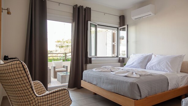 Een slaapkamer met een bed, een stoel, een raam met gordijnen en een airconditioning.