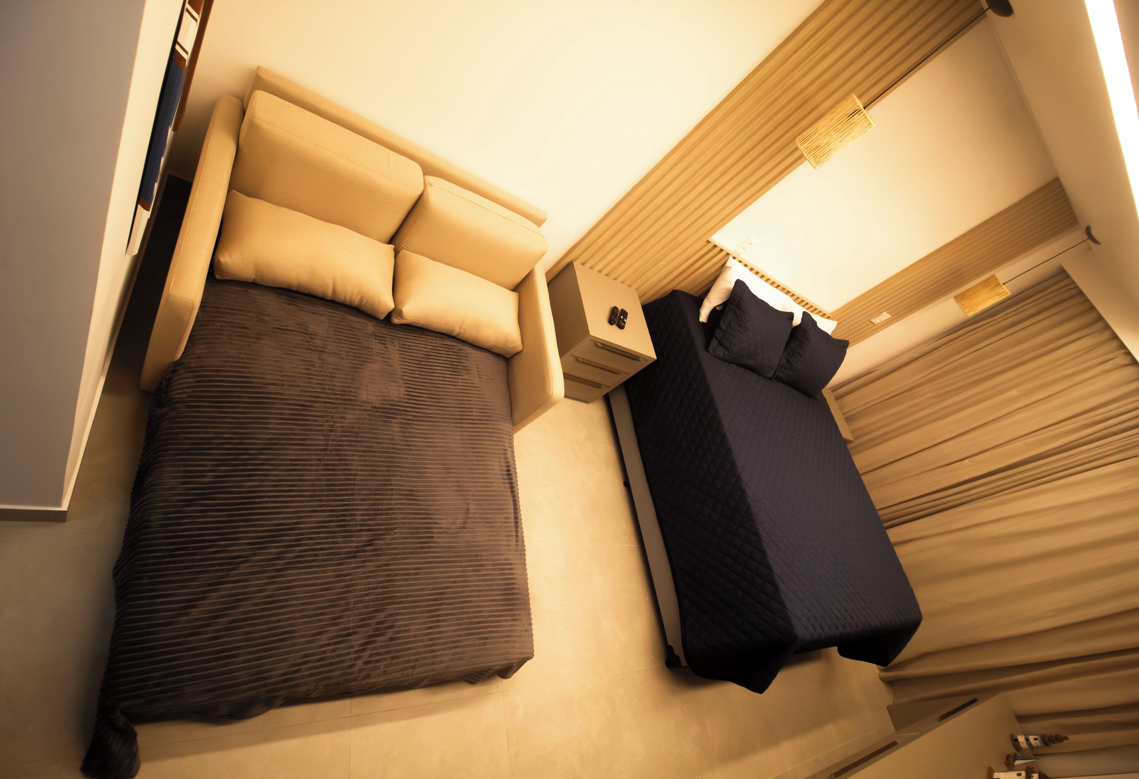 A compact hotel room with a bed, a small bedside table, a nightstand, and a window with curtains.