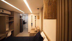 A bedroom with a bed, a desk, a chair, a wardrobe, a hanging light fixture, and a wall-mounted decorative item. - FLAT BEACH CLASS SUMMER - PORTO (Ipojuca)