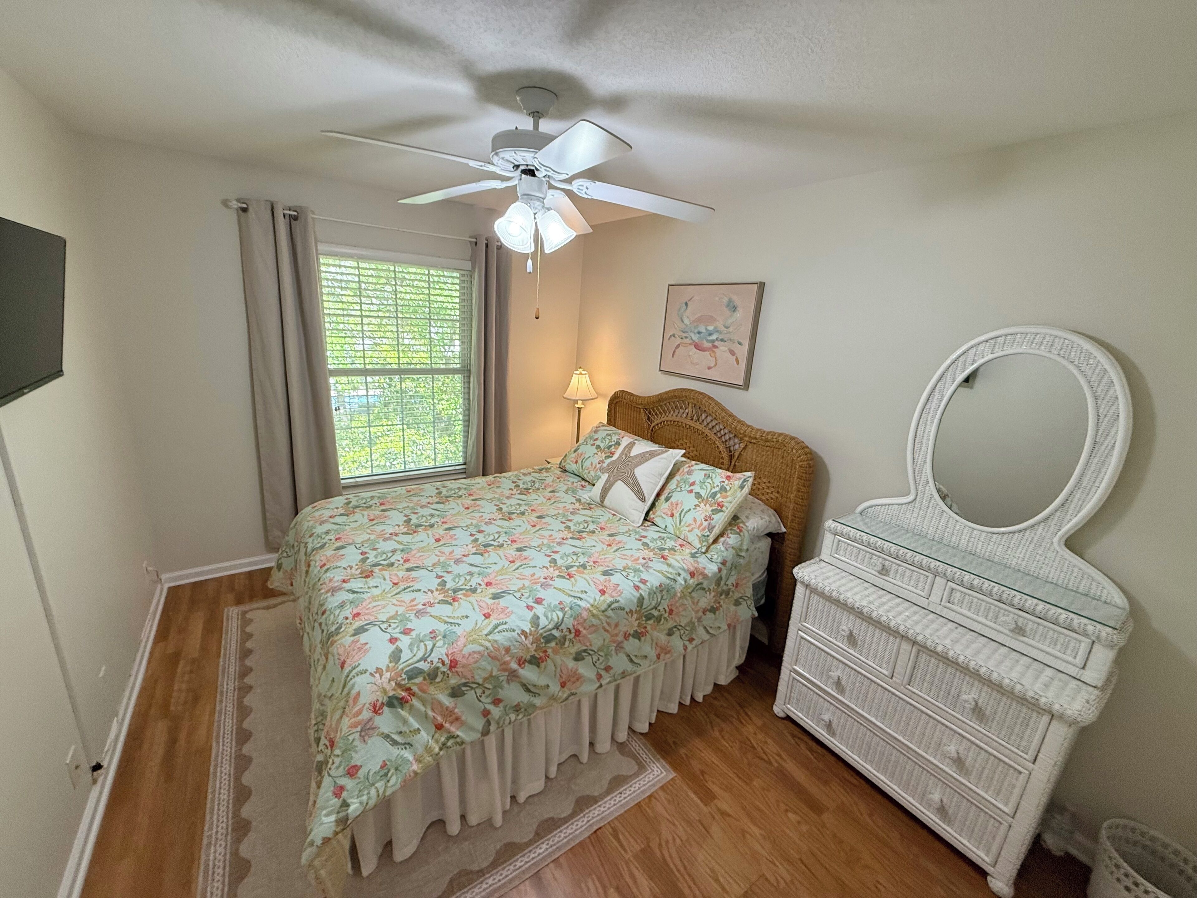 Un dormitorio con cama, cómoda, ventilador de techo, ventana con cortinas y una lámpara de pared.