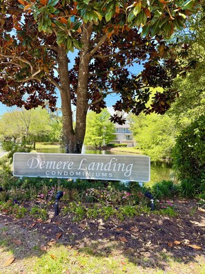 Schild für Demere Landing Condominiums, im Hintergrund ein Teich und Bäume.