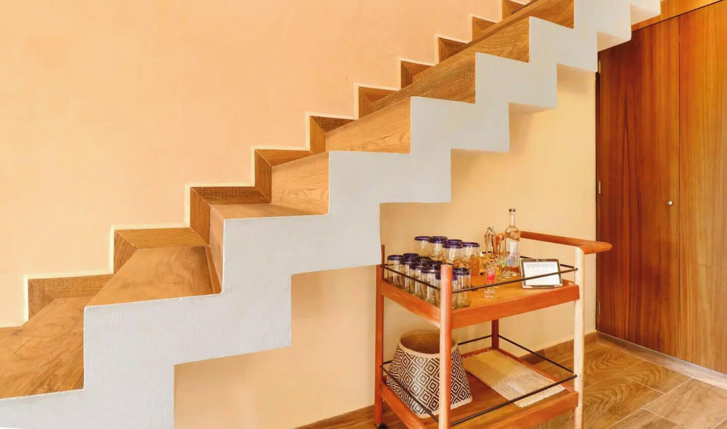 A staircase with wooden steps and white risers, leading to a wooden door. A shelf with jars and a candle is placed beside the stairs.