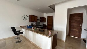 Una cucina moderna con un piano di lavoro in granito, elettrodomestici in acciaio inossidabile e uno sgabello da bar nero.