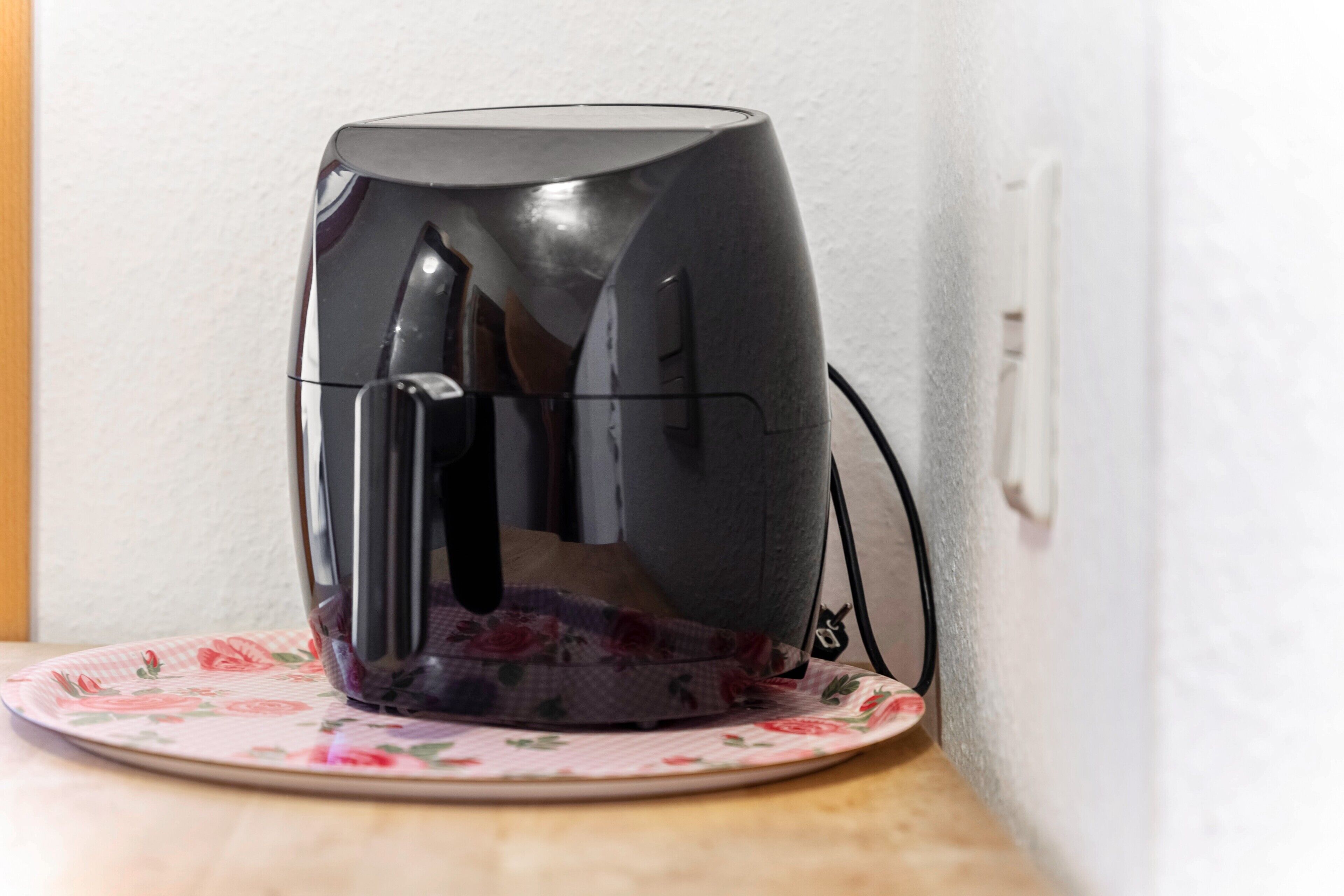 Une machine à café noire posée sur une assiette à motifs floraux.