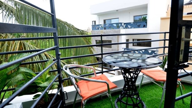 Un balcone con un tavolo e sedie in vetro, immerso nel verde con un edificio moderno sullo sfondo.