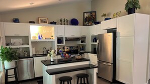 A modern kitchen with white cabinets, a black countertop, stainless steel appliances, and a small island with stools.