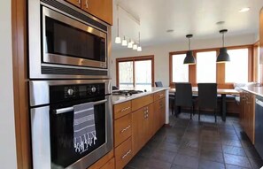 A kitchen with stainless steel appliances, wooden cabinets, a dining area with chairs, and pendant lights. - The Country House (Culver)