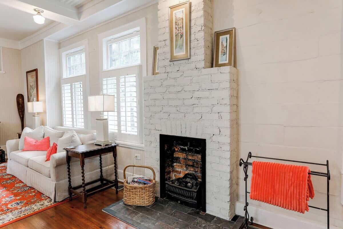 Una sala de estar con chimenea de ladrillo blanco, un sofá, una mesa y una alfombra.