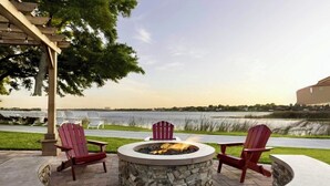 A circular stone fire pit with two Adirondack chairs, a pergola, and a view of a body of water. - Orlando Studio Villa Near Disney - Westgate Lakes (Orlando)