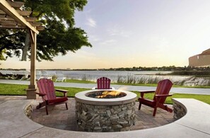 A circular stone fire pit with two Adirondack chairs, a pergola, and a view of a body of water. - Orlando Studio Villa Near Disney - Westgate Lakes (Orlando)