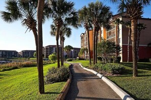 A pathway lined with palm trees leading to a building with multiple floors and large windows. - Orlando Studio Villa Near Disney - Westgate Lakes (Orlando)