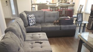 En modulsofa med en fjernbetjening, et spisebord og et køkken i baggrunden.