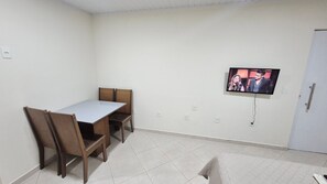 A room with a dining table and chairs, a television mounted on the wall, and a door. - Residencial Riviera Apartamentos (Vila Velha)