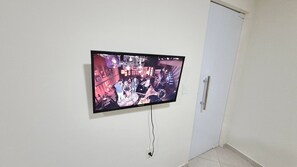 A television mounted on a wall in a room with a door and a tiled floor. - Residencial Riviera Apartamentos (Vila Velha)