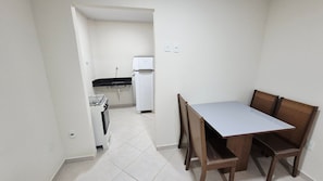 A small kitchen with a gas stove, a refrigerator, and a dining table with chairs. - Residencial Riviera Apartamentos (Vila Velha)