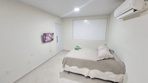 A bedroom with a bed, a TV mounted on the wall, and an air conditioning unit. - Residencial Riviera Apartamentos (Vila Velha)