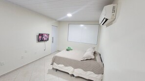 A bedroom with a bed, a television mounted on the wall, and an air conditioning unit. - Residencial Riviera Apartamentos (Vila Velha)