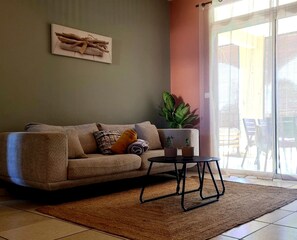 Una sala de estar con un sofá, una mesita, una planta en maceta y un ventanal corredera.