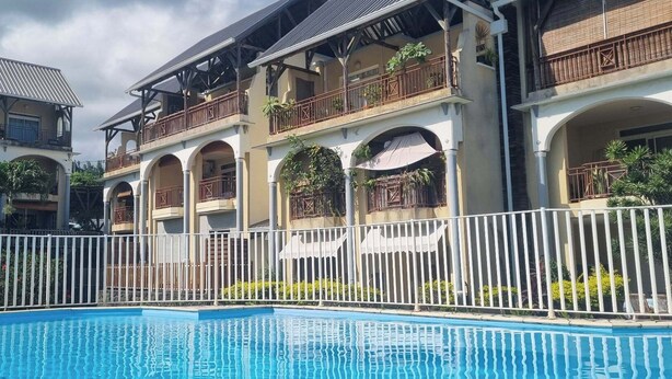 Une piscine entourée d’une clôture blanche, elle-même bordée d’immeubles à plusieurs étages dotés de balcons et de fenêtres en arc de cercle.