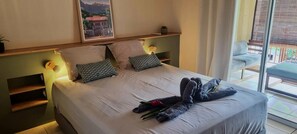Una cama bien hecha con almohadas, una toalla y una flor roja, un cuadro en la pared y un balcón con vistas.